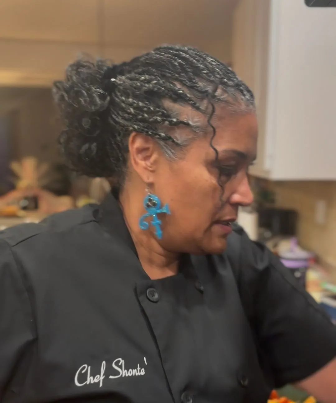 Chef Shonte in black chef's coat with braided updo and blue earrings working in kitchen