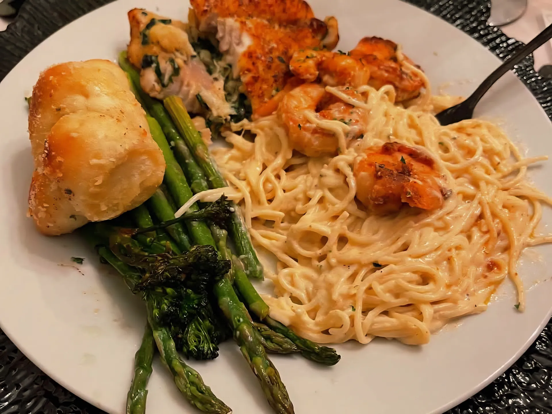 Plated dinner with pan-seared chicken, shrimp pasta in cream sauce, and roasted asparagus on white dish