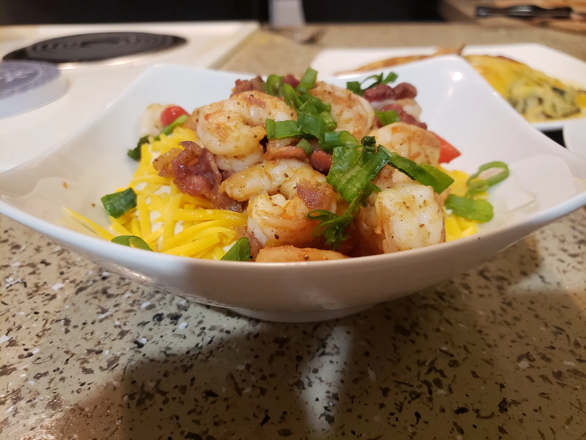 Seasoned shrimp with bacon and green onions served over yellow cheese grits in a white square bowl
