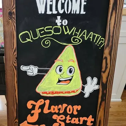 Chalkboard sign with smiling quesadilla character welcoming customers to QuesoWhaat!?! Flavor Forward
