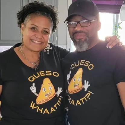 Smiling couple wearing matching black t-shirts with QuesoWhaat!?! logo featuring cartoon cheese wedge character