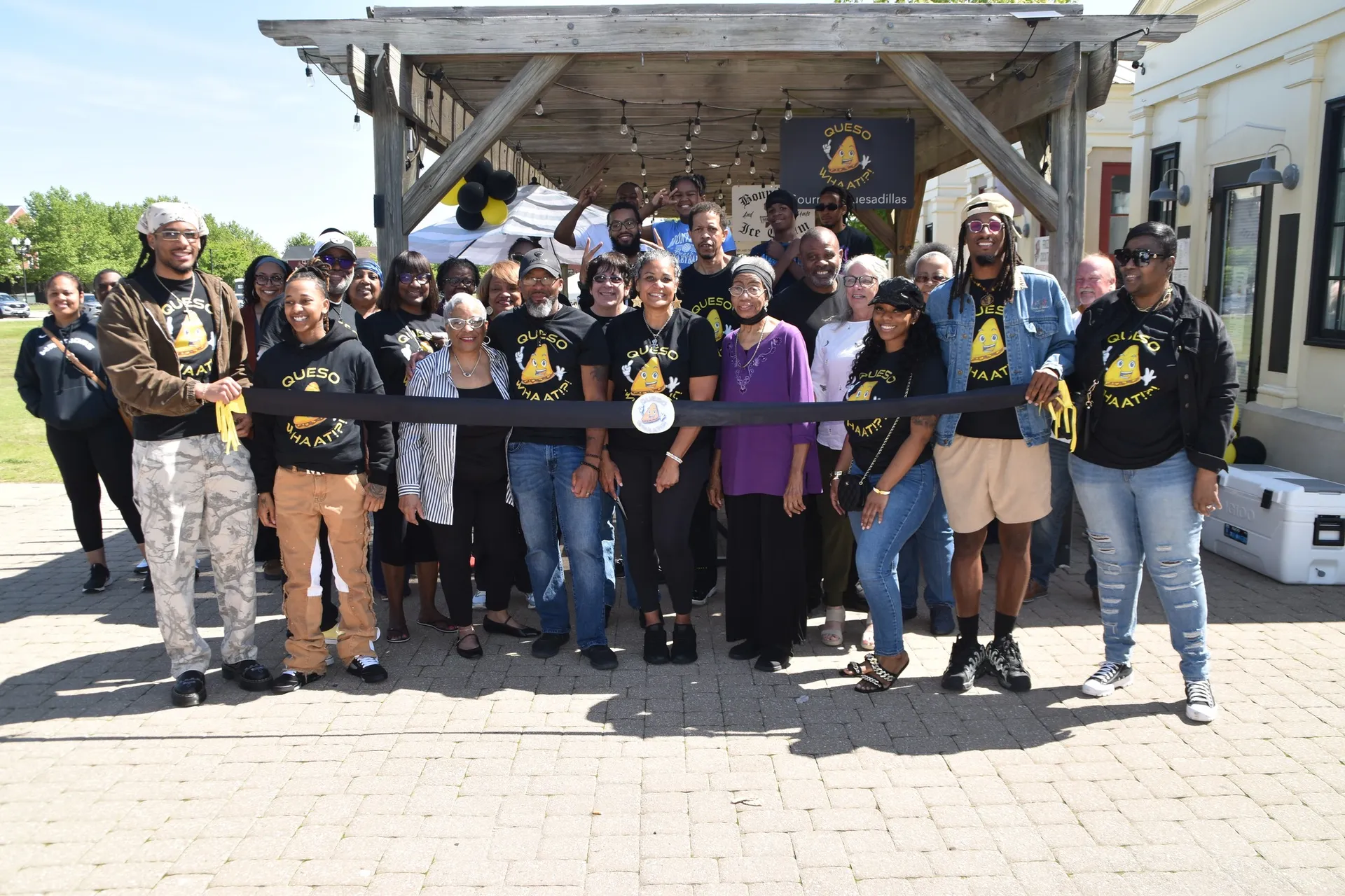 Large group photo of Whaat!?! Foods team members wearing matching black QuesoWhaat shirts at outdoor event venue