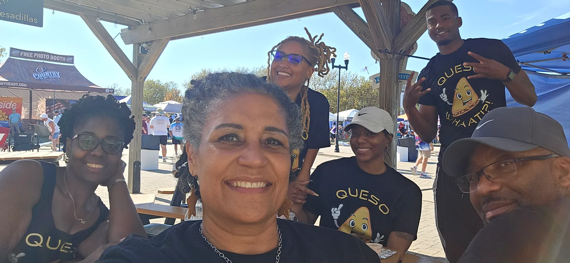 Team of six people wearing matching navy QUESO branded t-shirts smiling at outdoor event booth
