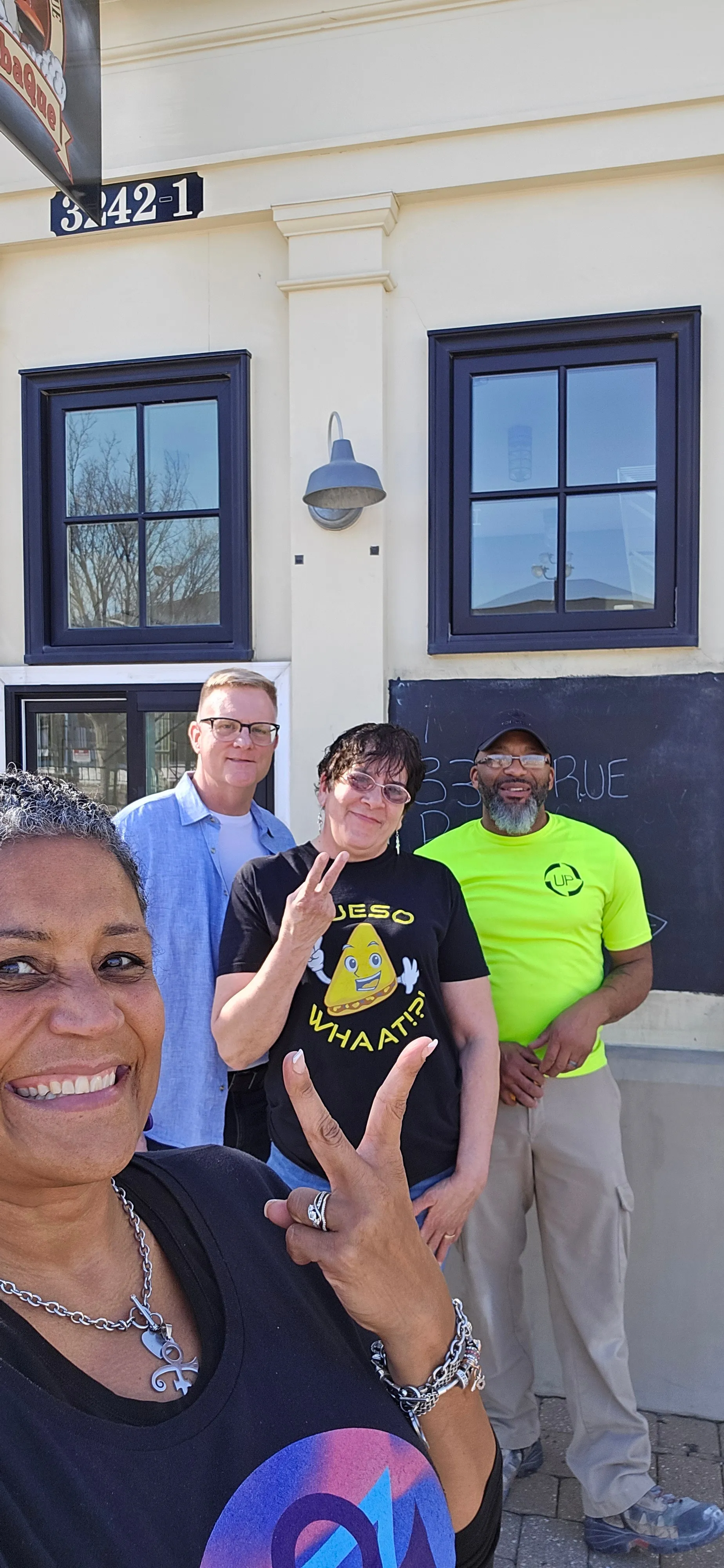 Four smiling team members posing outside Whaat!?! Foods restaurant storefront with navy-trimmed windows and address 3A42-1